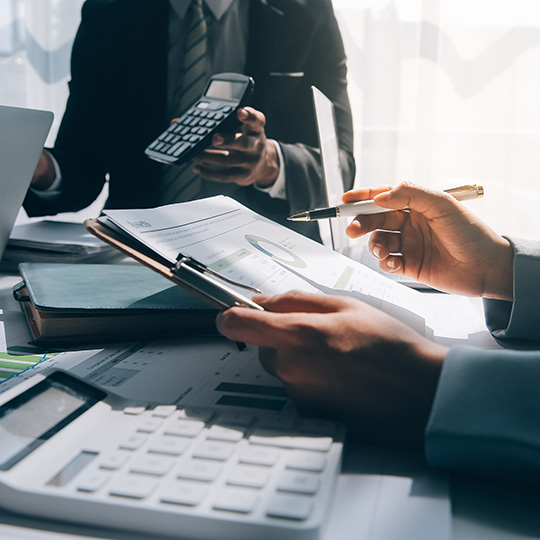 A business meeting with professionals discussing financial reports while using a calculator, pen, and documents on the table.