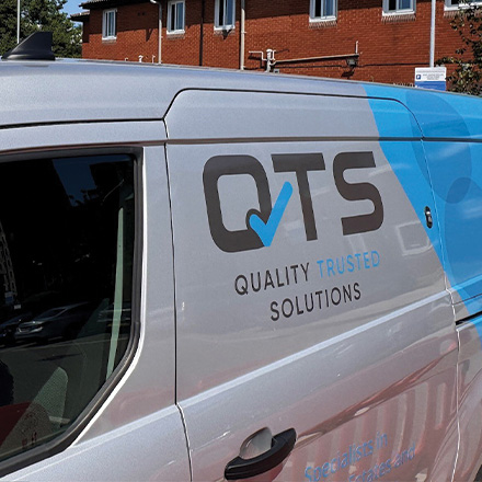 A side view of a delivery van featuring the logo and branding of QTS, which includes the words 