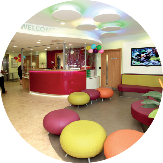 A colorful and inviting reception area with circular seating, modern decor, and a large aquarium, showcasing a warm welcome in a healthcare setting.