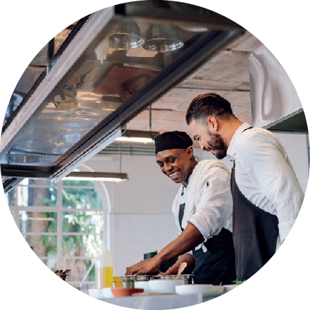 Two male chefs collaborating in a bright kitchen, preparing ingredients with professional cooking tools.