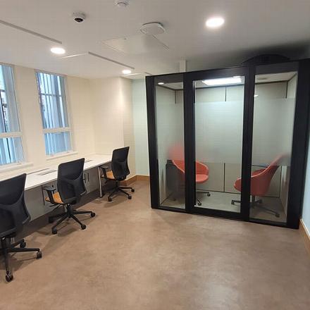 Modern office space with four ergonomic chairs at desks and a glass meeting room featuring two orange chairs, designed for collaborative work.