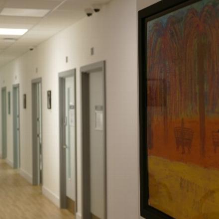 a corridor with several doors on either side, featuring a colorful artwork of trees on the wall, conveying a serene and inviting atmosphere in a healthcare facility