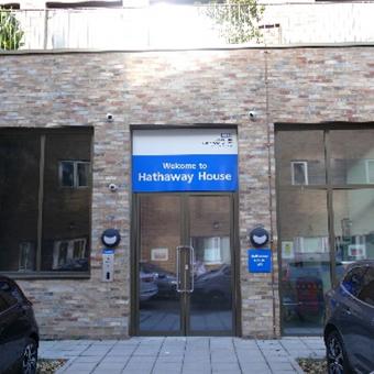 Entrance to Hathaway House featuring a welcoming sign, surrounded by a modern brick facade and parked vehicles. The image captures the contemporary architecture and inviting atmosphere.