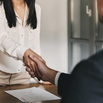 Handshake between two individuals at a desk, with a signed contract visible below, representing professional agreement and partnership.