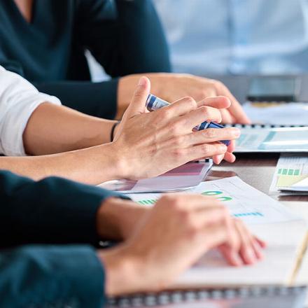 Hands engaged in discussion during a meeting, with paperwork and charts visible on the table.